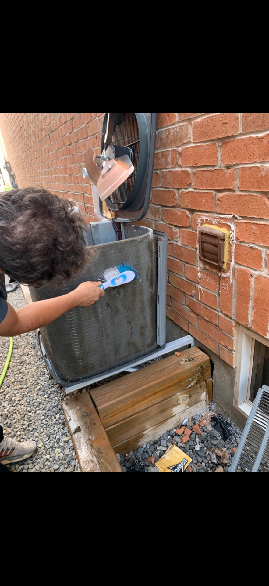 Technician brushing condenser coils of an outdoor AC unit